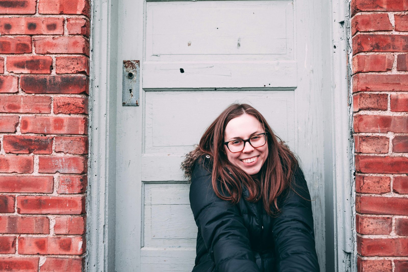 smiling woman sits beside white wooden door during daytime